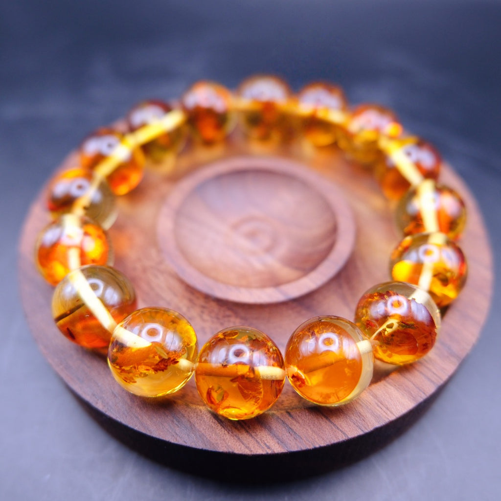 Bracelet: transparent golden-orange amber beads with flower-like inclusions, on a wooden dish