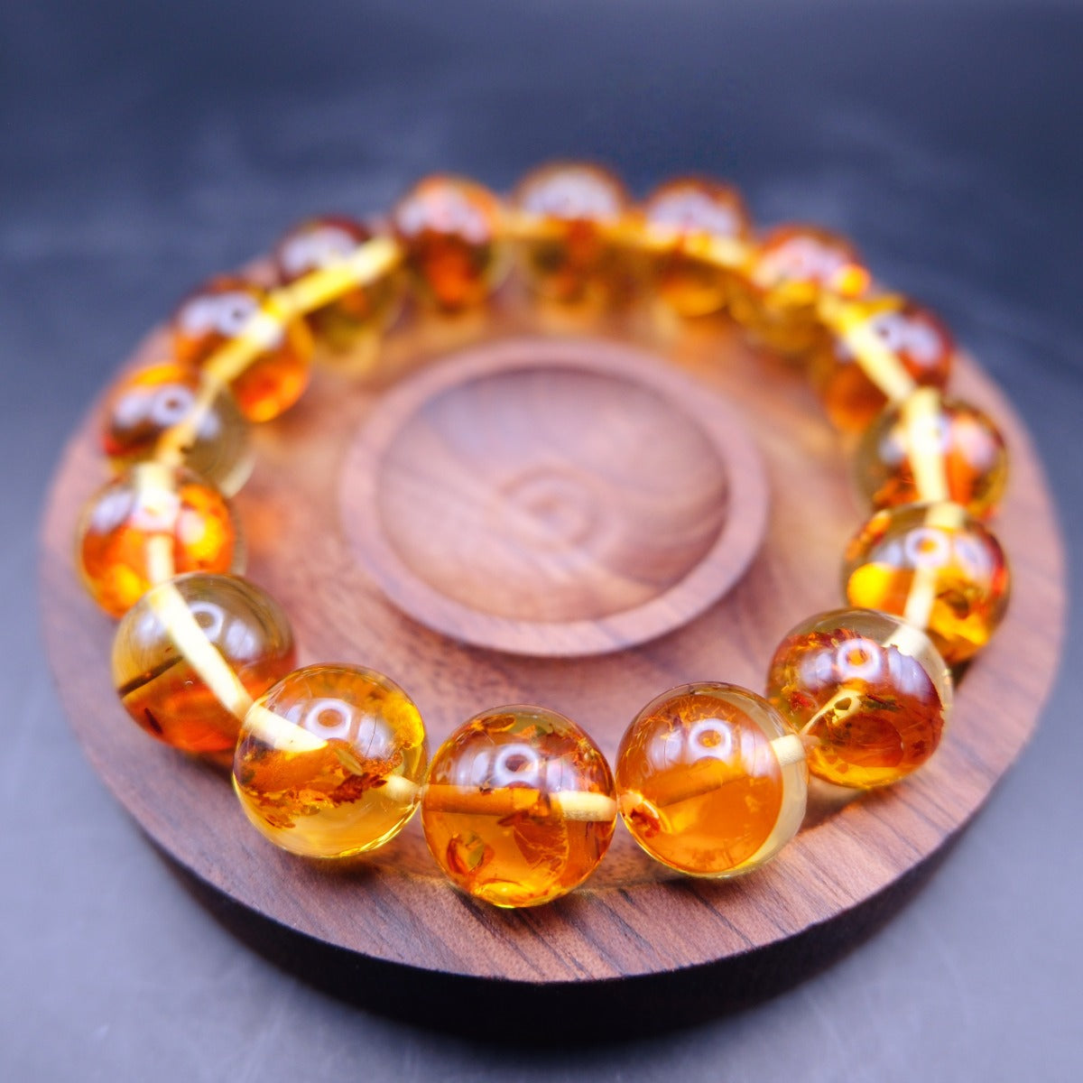 Bracelet: transparent golden-orange amber beads with flower-like inclusions, on a wooden dish