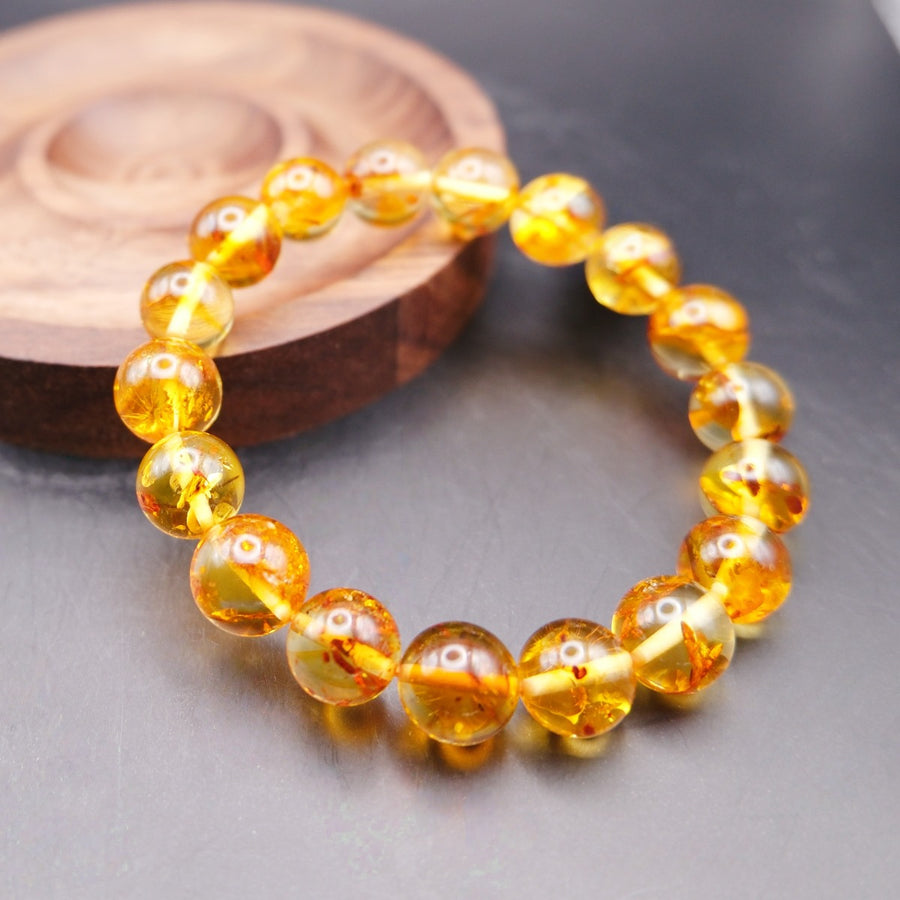 Bracelet: transparent golden-yellow amber beads with small inclusions, beside a wooden dish