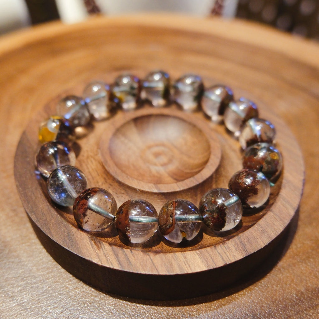 Bracelet: clear phantom quartz beads with red-brown inclusions, in a wooden dish