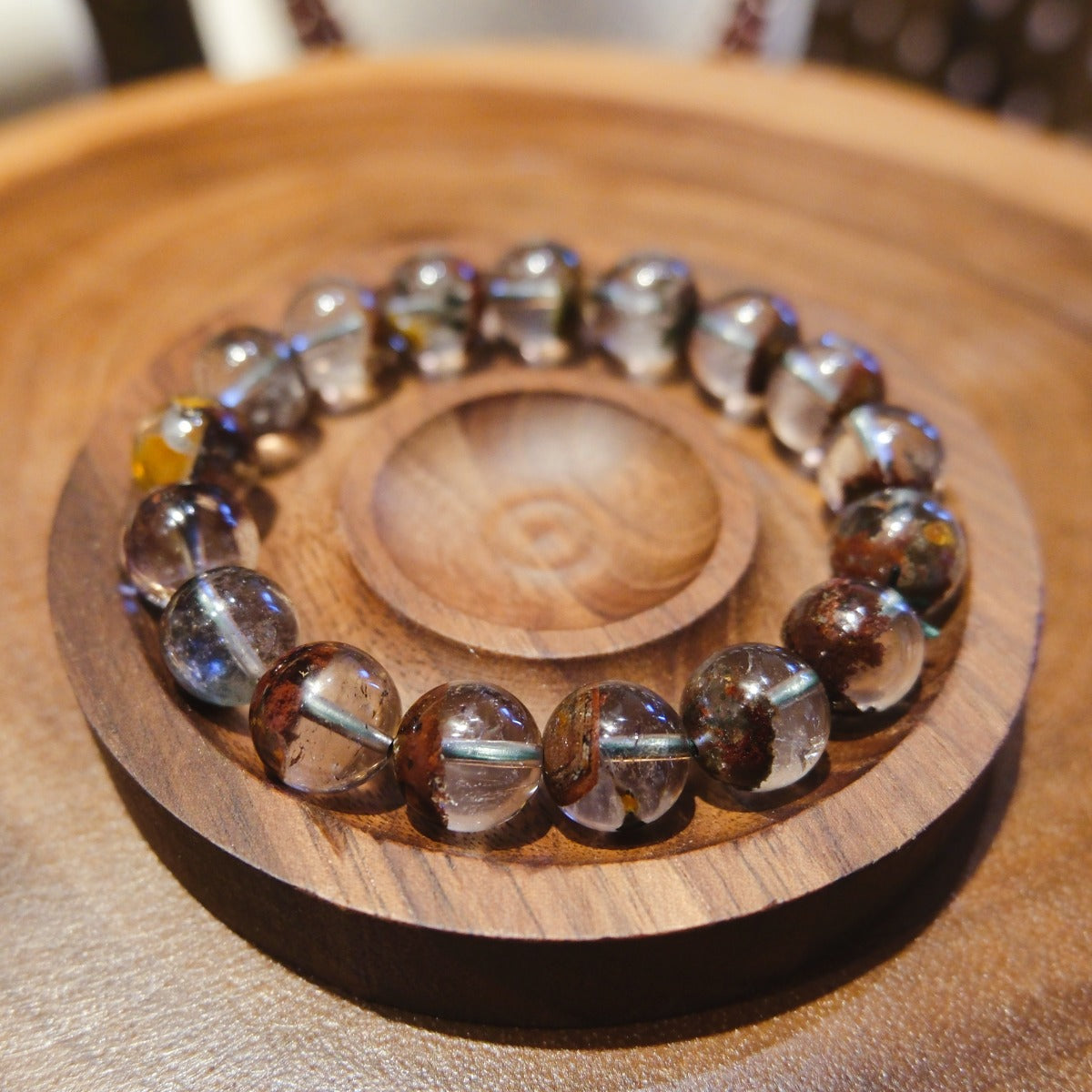 Bracelet: clear phantom quartz beads with red-brown inclusions, in a wooden dish