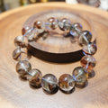 Bracelet: clear phantom quartz beads with red-brown and green inclusions, on a wooden dish