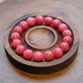Bracelet: round pink rhodonite beads in a dark wooden dish