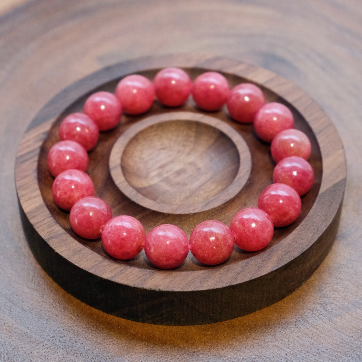 Bracelet: round pink rhodonite beads in a dark wooden dish