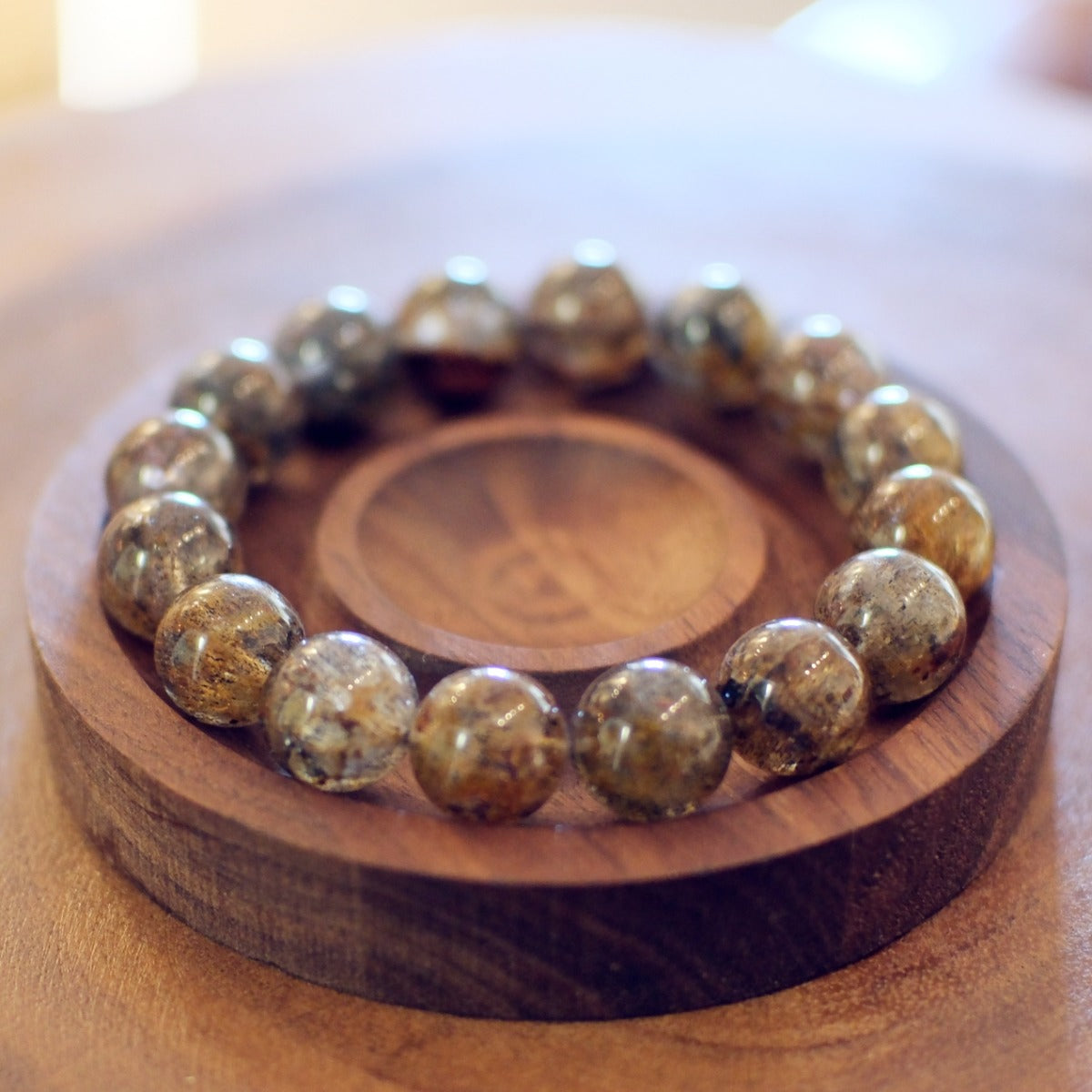Bracelet: Super Seven beads, clear grey with dark and golden inclusions, in a wooden dish