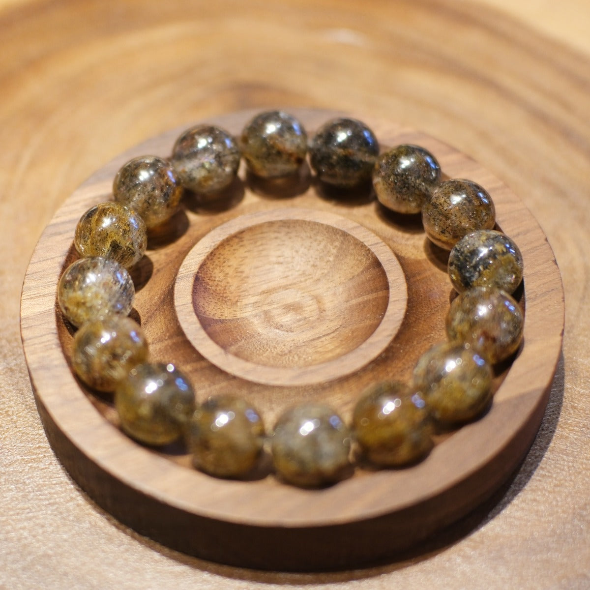 Bracelet: Super Seven beads, clear grey with dark and golden inclusions, seen from above in a wooden dish