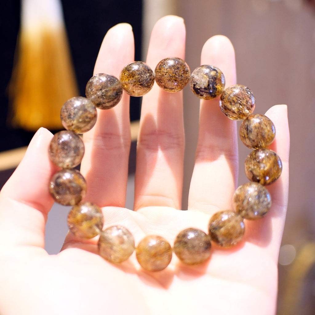 Bracelet: Super Seven beads, clear grey with dark and golden inclusions, held on an open palm