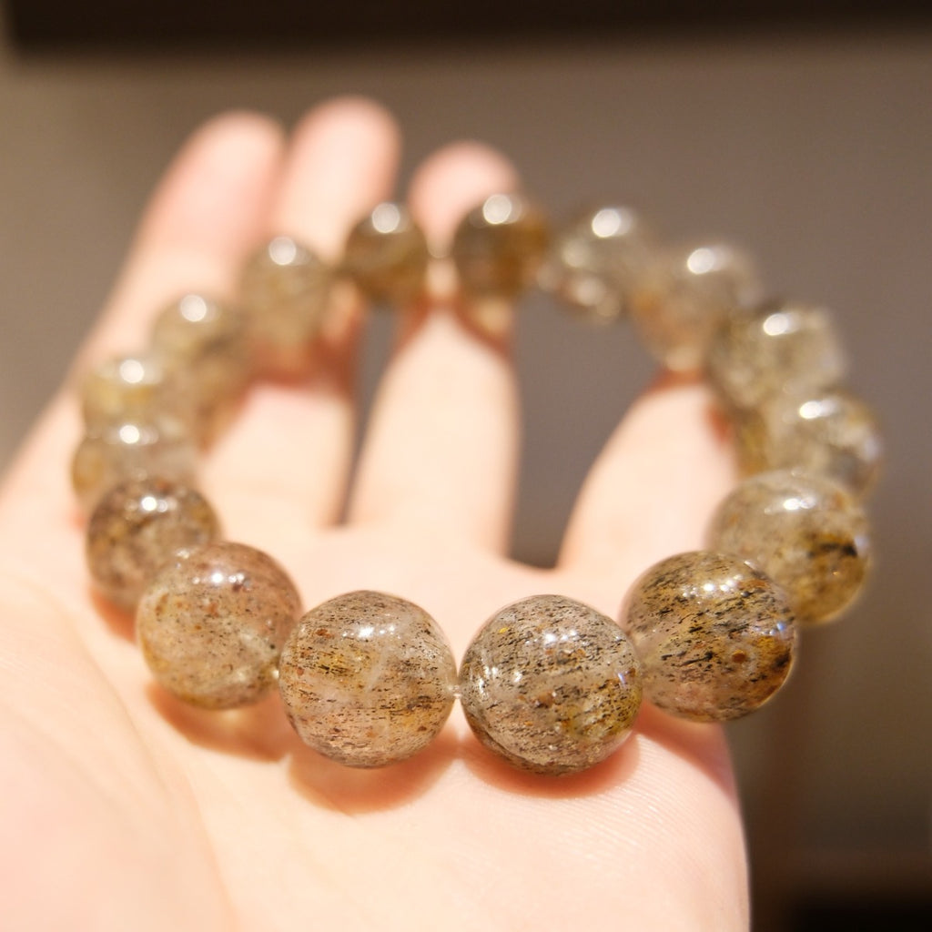 Bracelet: Super Seven beads, clear grey with dark and golden inclusions, held on an open palm