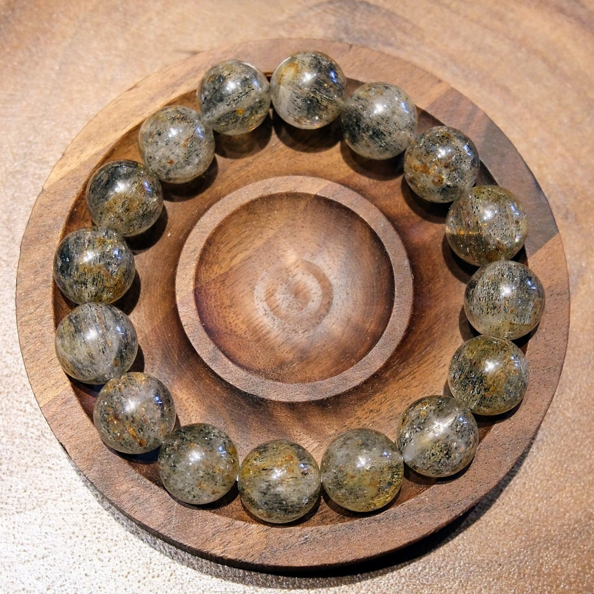 Bracelet: Super Seven beads, clear grey with dark and golden inclusions, seen from above in a wooden dish