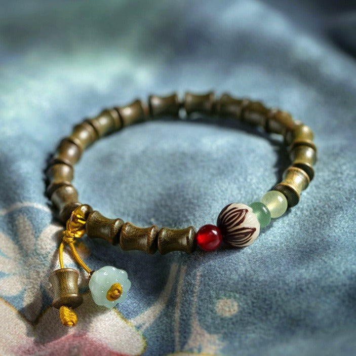 Bracelet: olive-brown sandalwood beads shaped like bamboo segments, with a red bead, a lotus bead and pale green beads