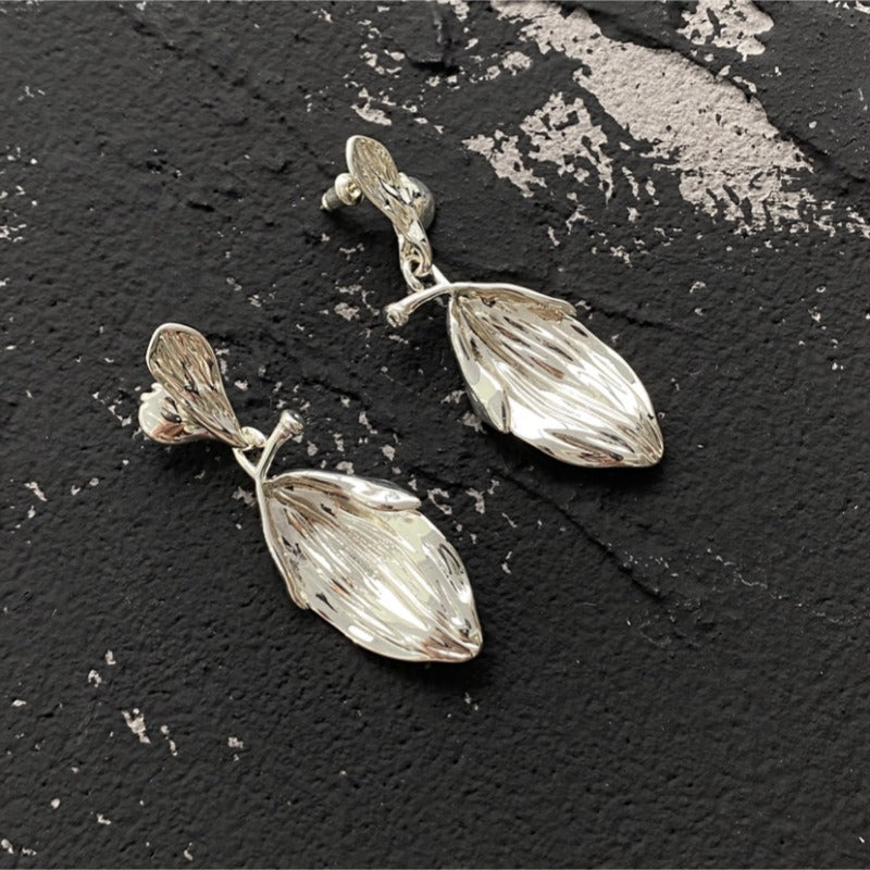 Earrings: silver drop earrings, a small textured stud with a larger ribbed leaf-shaped drop, on a dark background