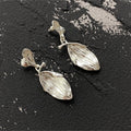 Earrings: silver drop earrings, a small textured stud with a larger ribbed leaf-shaped drop, on a dark background