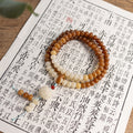 Mala: 108 brown bodhi root disc beads with a run of cream beads, wound in loops on a printed page