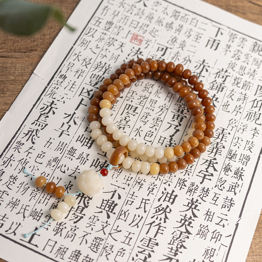 Mala: 108 brown bodhi root disc beads with a run of cream beads, wound in loops on a printed page
