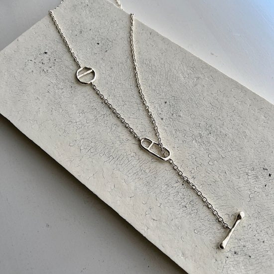 Necklace: long polished 925 sterling silver chain with two oval links and a T-bar toggle, laid on a pale stone slab