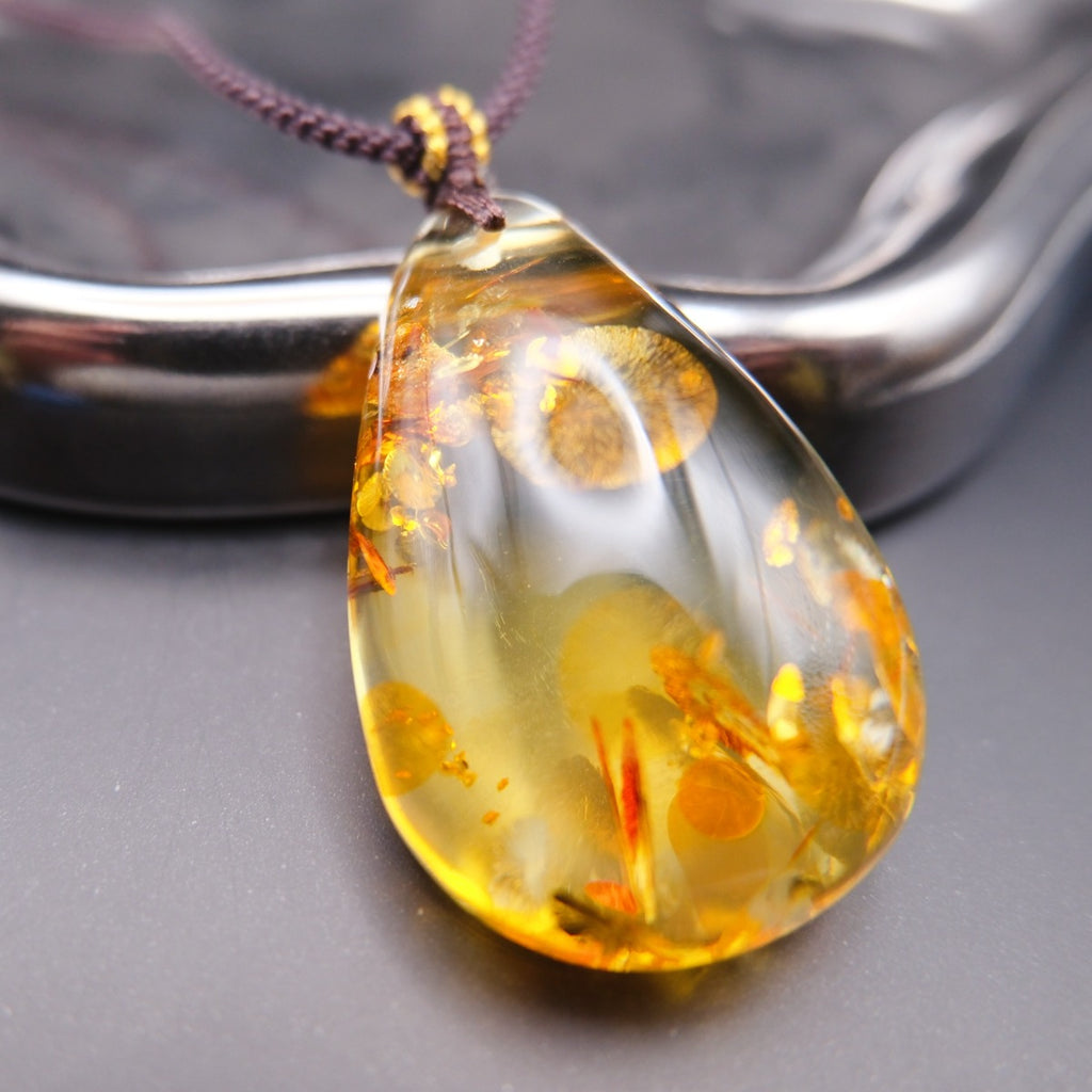 Pendant: golden Baltic amber teardrop with round botanical inclusions, dark cord, closer view
