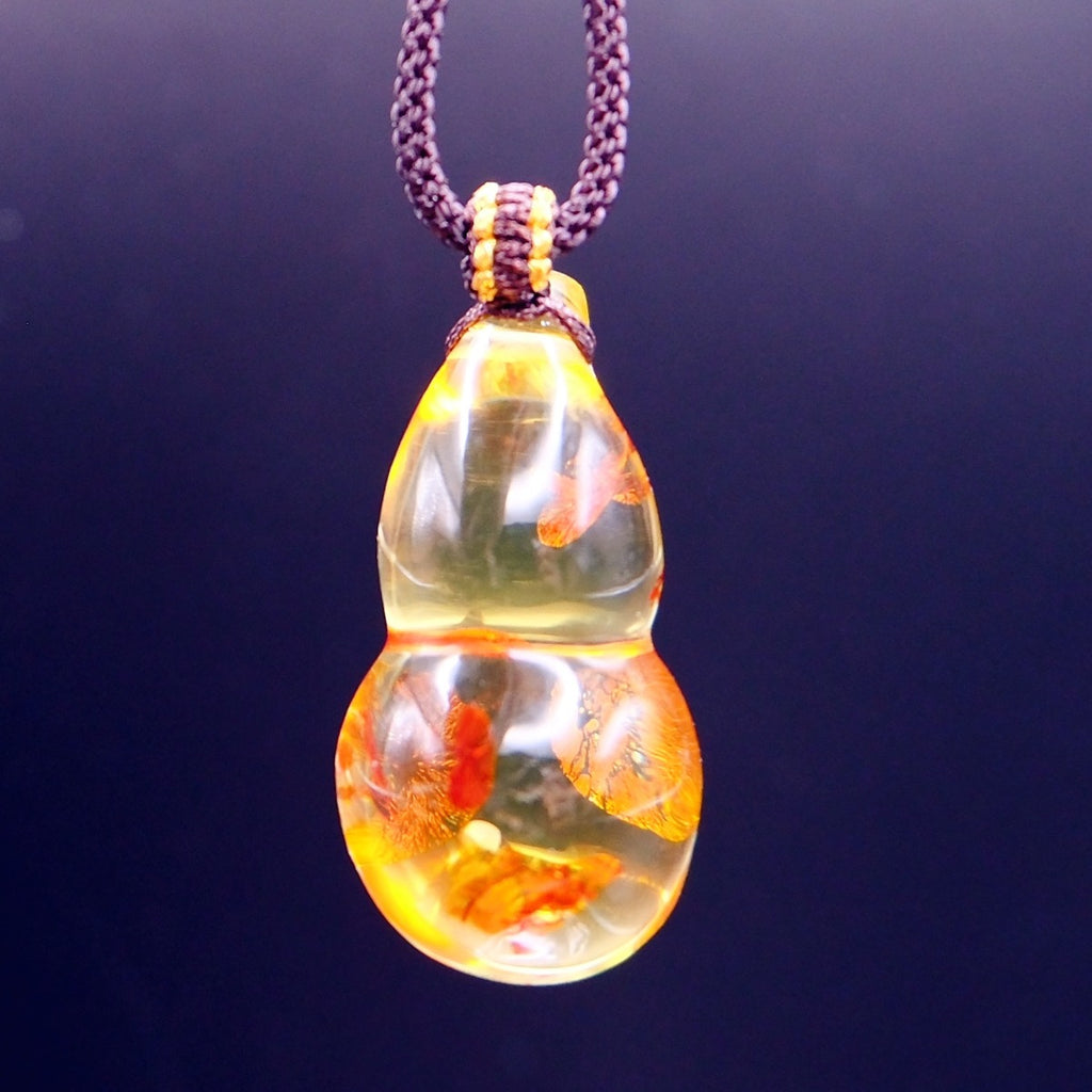 Pendant: golden Baltic amber gourd with orange-red inclusions, dark braided cord, hanging against a dark blue background