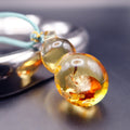 Pendant: transparent golden Baltic amber gourd with pale and orange inclusions, teal cord, lying by a metal tray