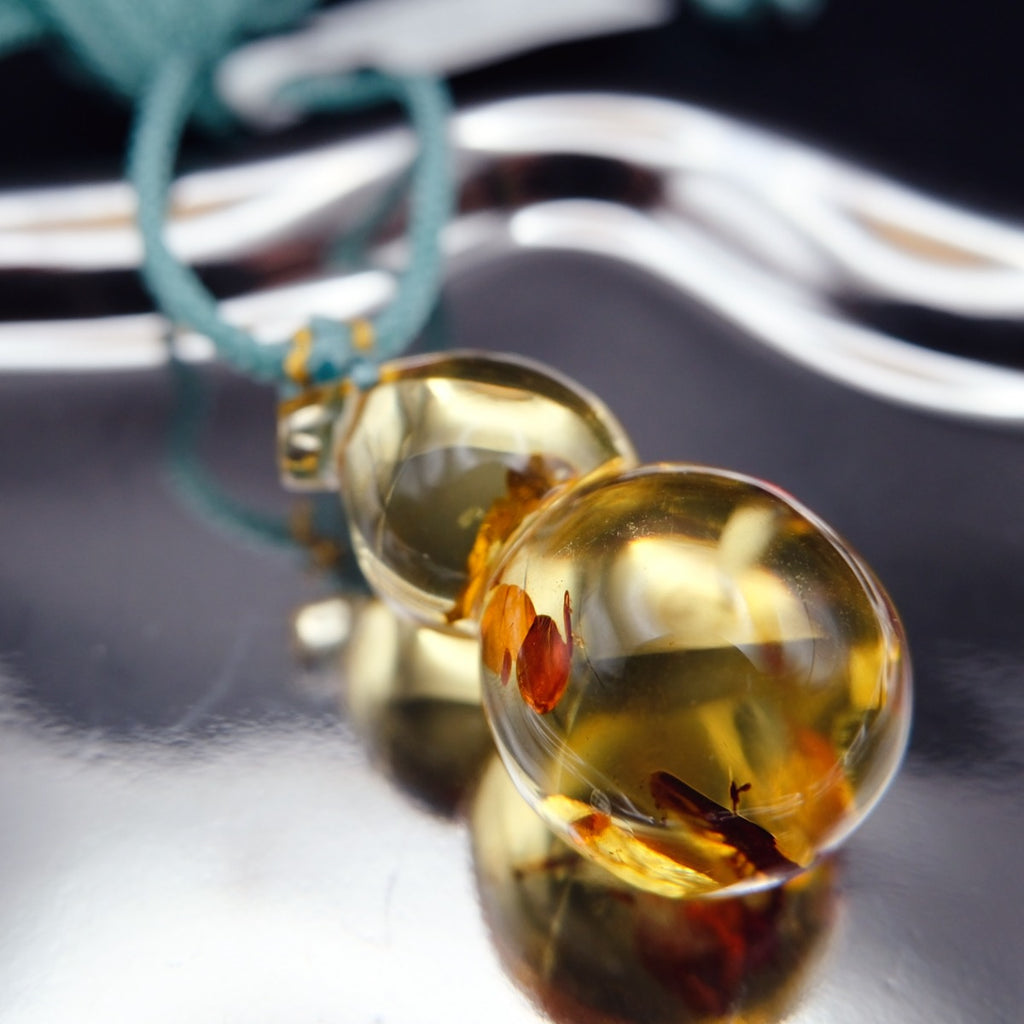 Pendant: transparent golden Baltic amber gourd with pale and orange inclusions, teal cord, close view of the lower bulb