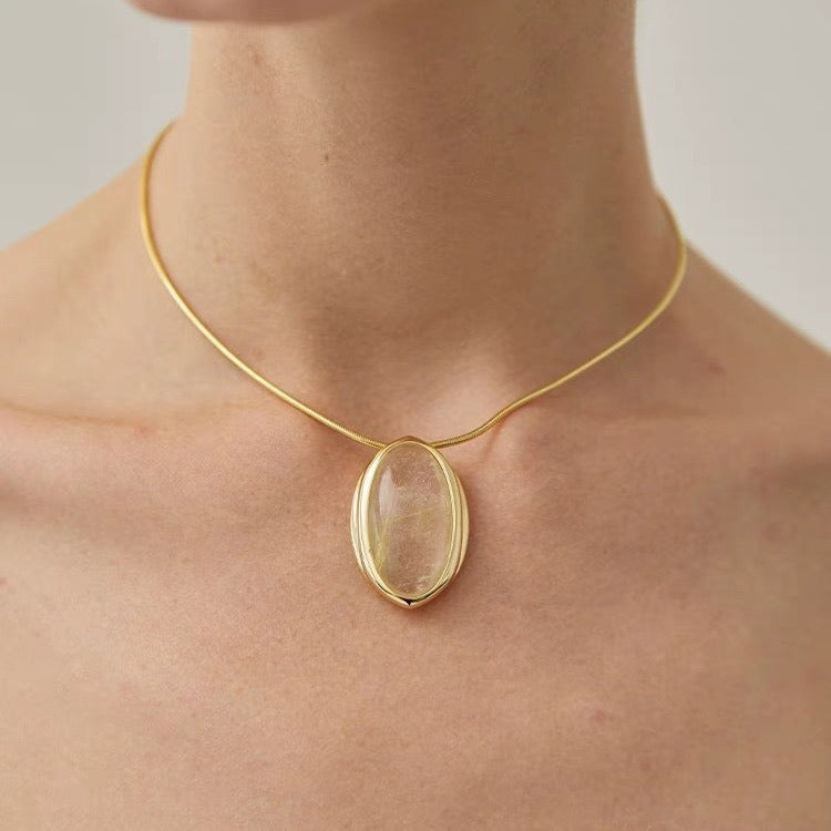 Pendant necklace: oval rutilated quartz cabochon in a gold-tone setting on a gold-coloured collar, worn at the neck