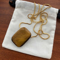Pendant necklace: golden-brown rectangular tiger's eye on a gold-coloured box chain, on a white pouch