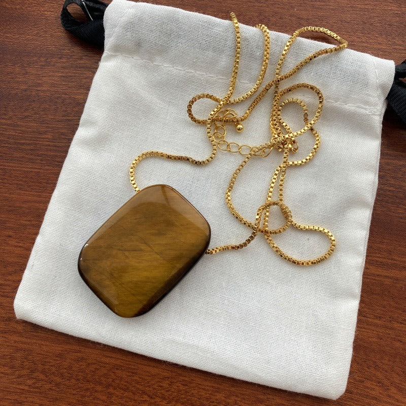 Pendant necklace: golden-brown rectangular tiger's eye on a gold-coloured box chain, on a white pouch