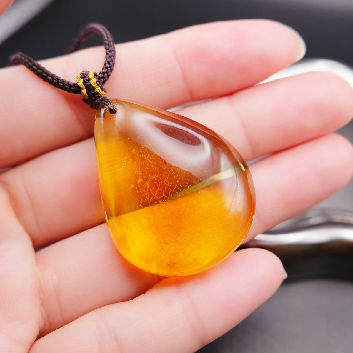 Pendant: transparent golden-yellow Baltic amber teardrop with a crackle-pattern inclusion, dark cord, on an open palm