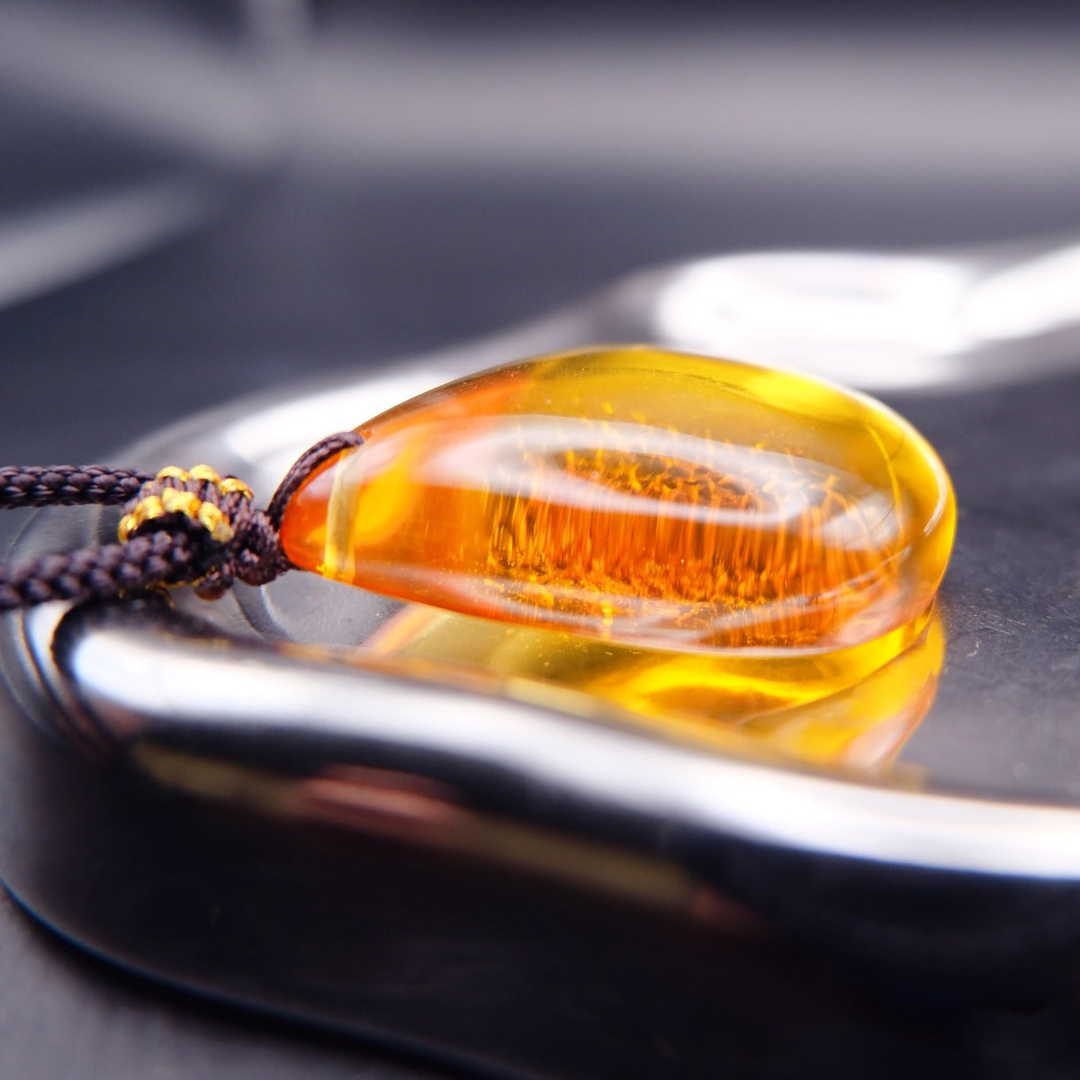 Pendant: transparent golden-yellow Baltic amber teardrop with a crackle-pattern inclusion, dark cord, lying, side view