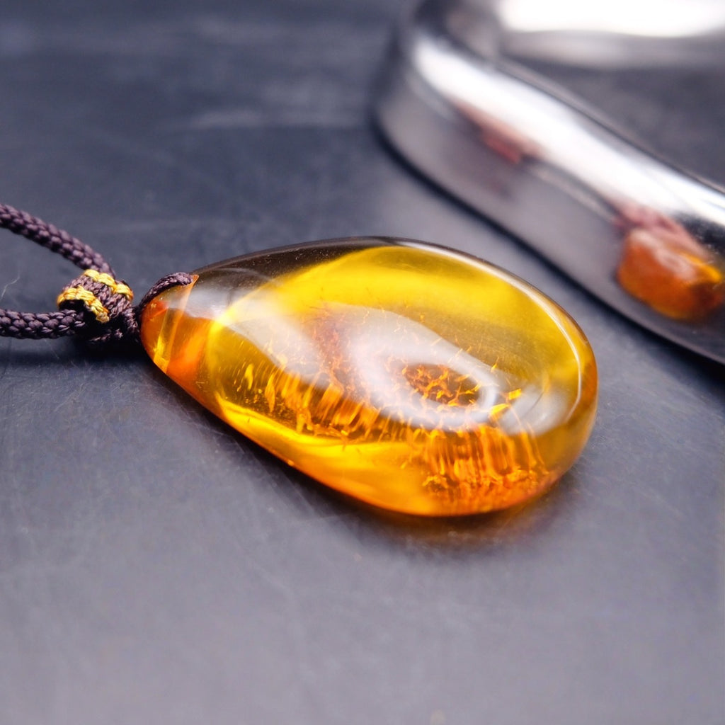 Pendant: transparent golden-yellow Baltic amber teardrop with a crackle-pattern inclusion, dark cord, lying flat