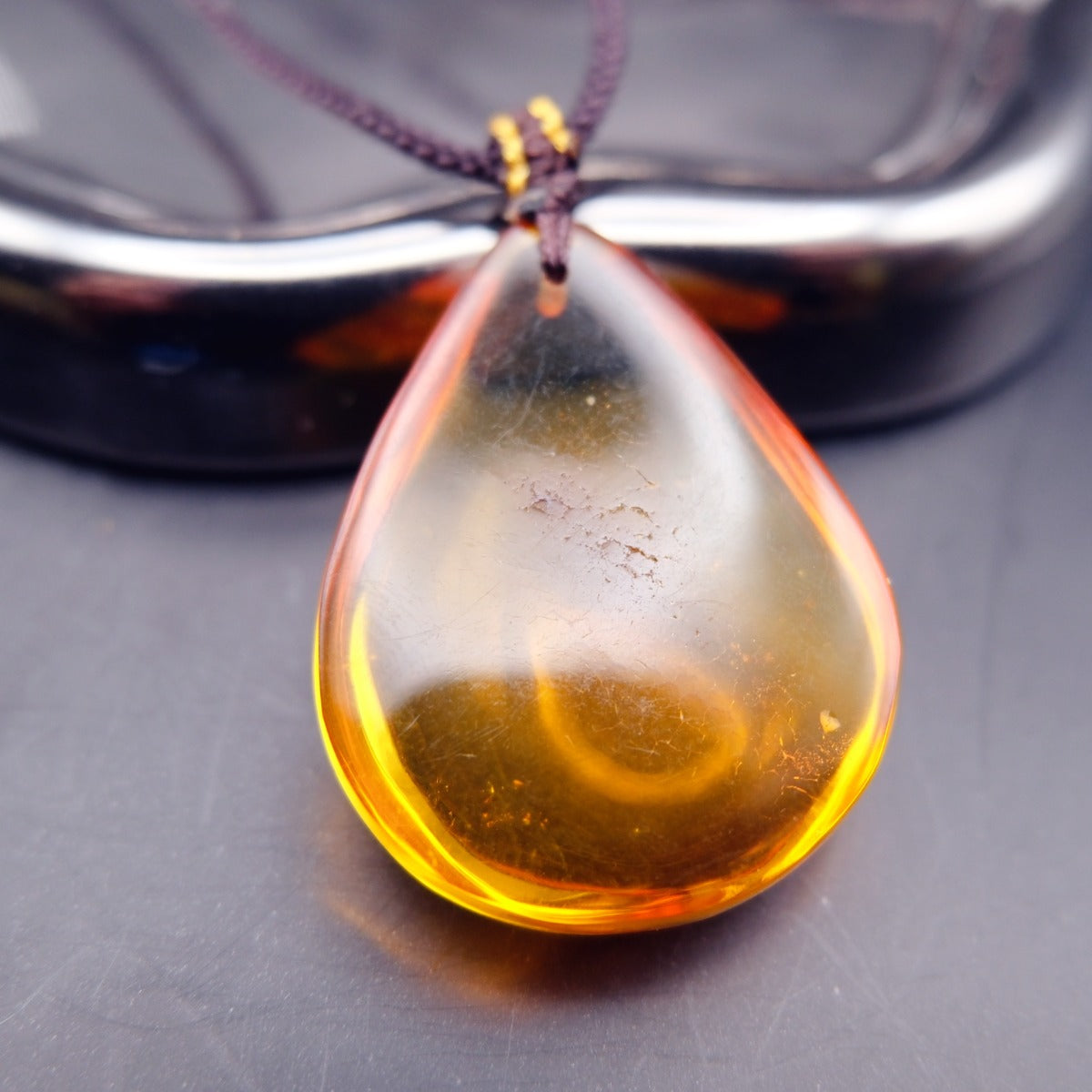 Pendant: transparent golden-yellow Baltic amber teardrop with a crackle-pattern inclusion, dark cord, leaning, front view