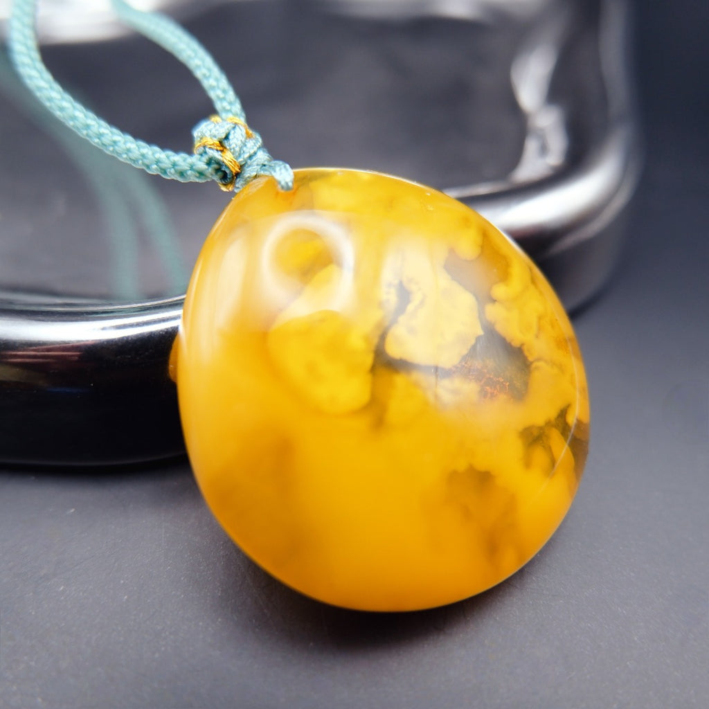 Pendant: opaque yellow-orange Baltic amber with paler cloud-like patches, teal cord, reverse side