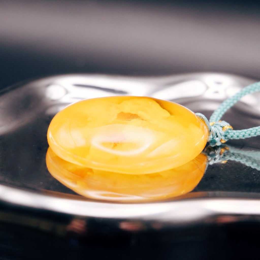 Pendant: opaque yellow-orange Baltic amber with paler cloud-like patches, teal cord, lying flat