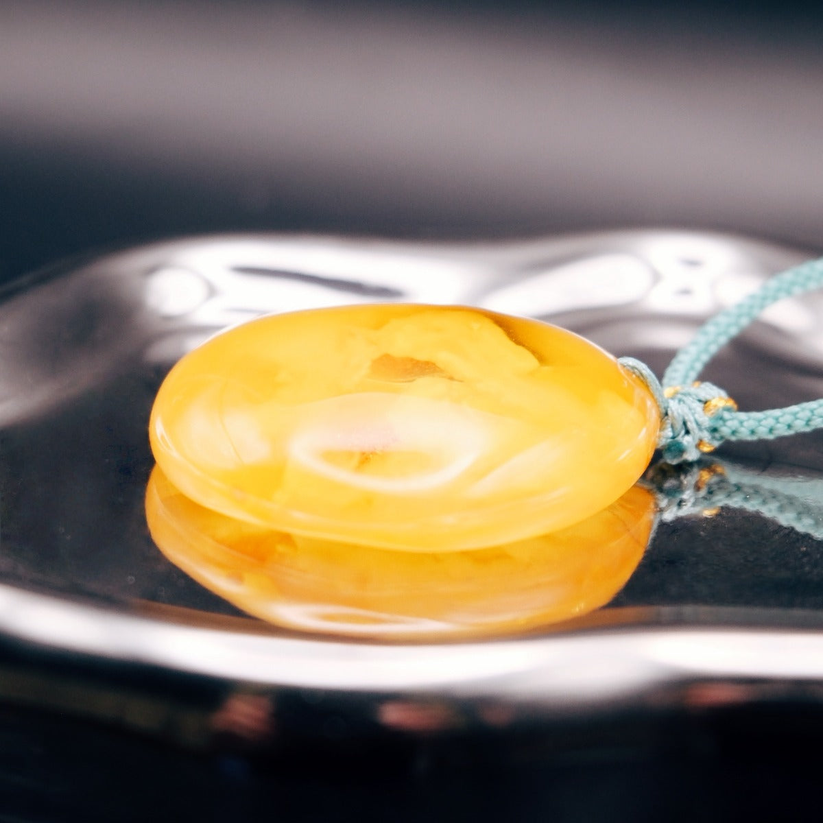 Pendant: opaque yellow-orange Baltic amber with paler cloud-like patches, teal cord, lying flat