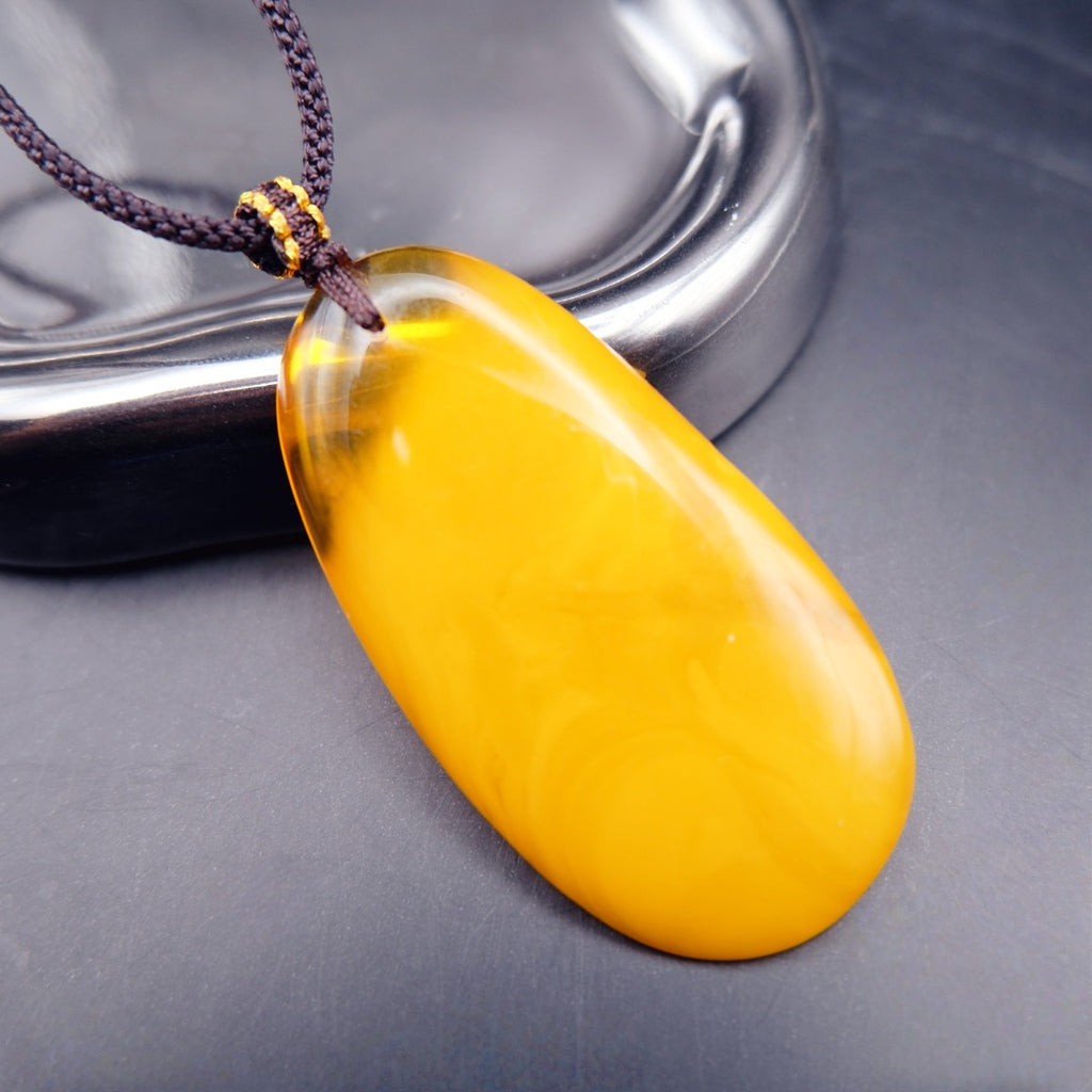 Pendant: long opaque yellow Baltic amber drop with a clear top edge, dark cord, lying by a metal tray