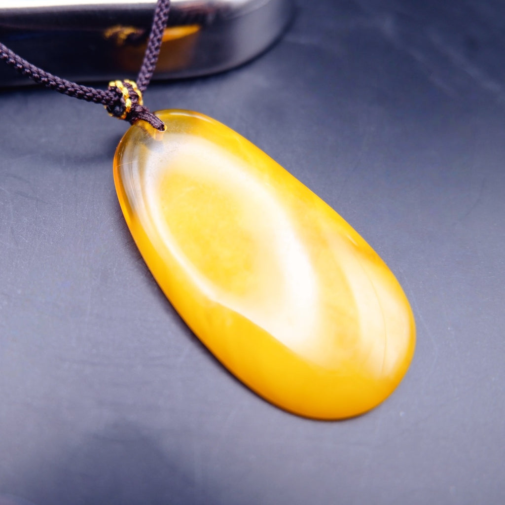 Pendant: long opaque yellow Baltic amber drop with a clear top edge, dark cord, second angle