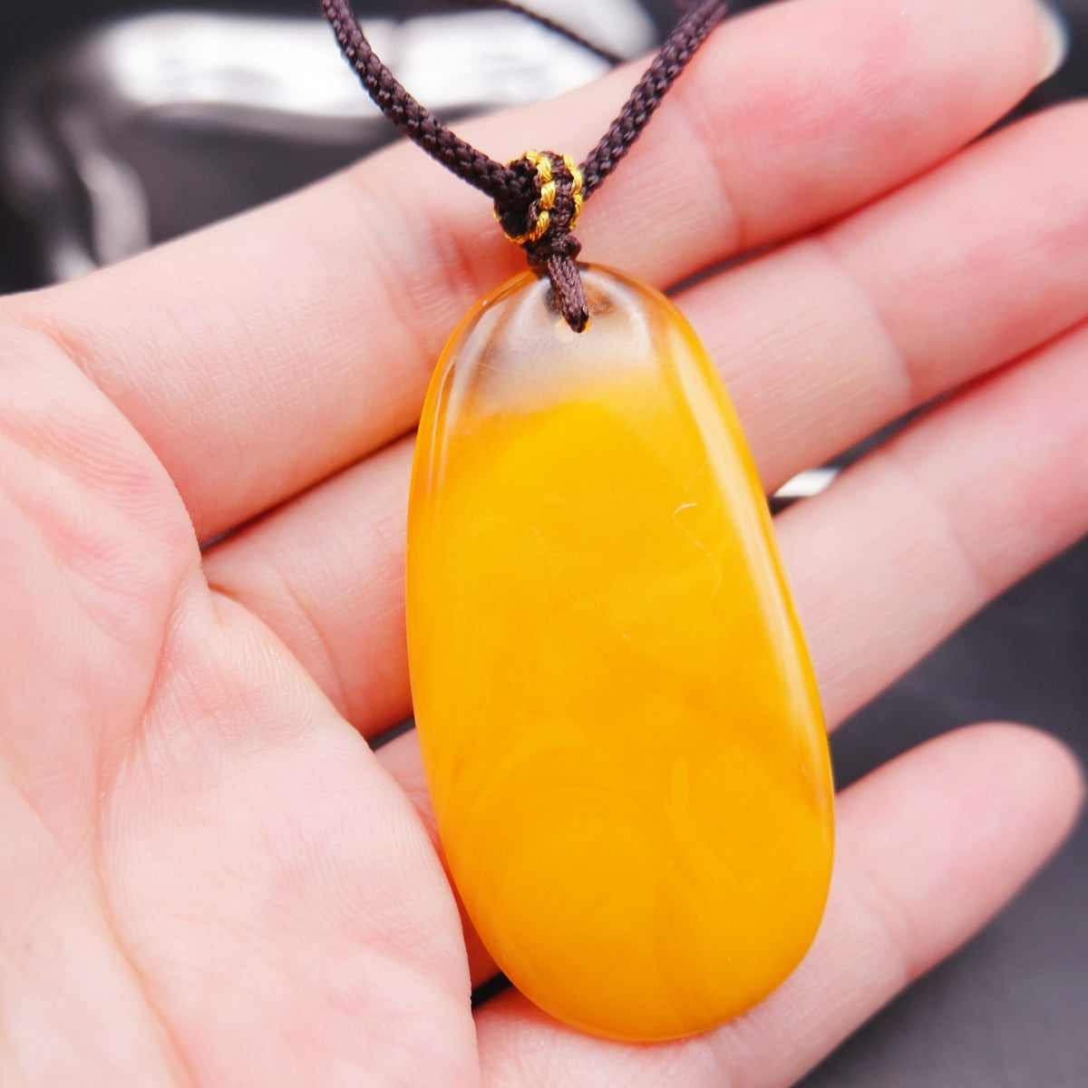 Pendant: long opaque yellow Baltic amber drop with a clear top edge, dark cord, on an open palm