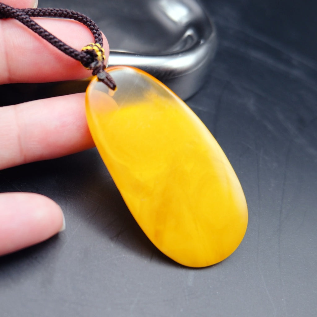 Pendant: long opaque yellow Baltic amber drop with a clear top edge, dark cord, held in fingers