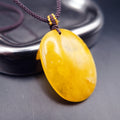 Pendant: yellow Baltic amber oval with cloudy white patches, dark cord, leaning on a metal tray