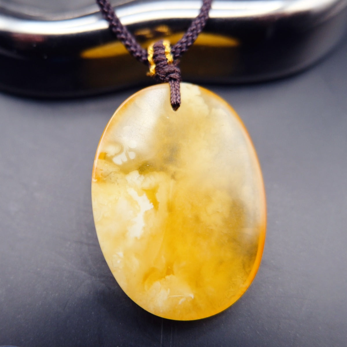 Pendant: yellow Baltic amber oval with cloudy white patches, dark cord, hanging, front view
