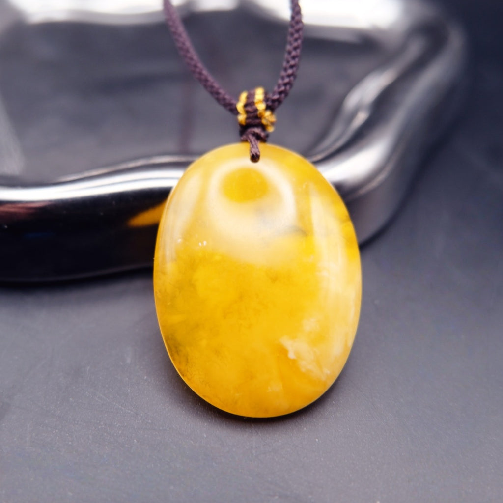 Pendant: yellow Baltic amber oval with cloudy white patches, dark cord, standing, front view