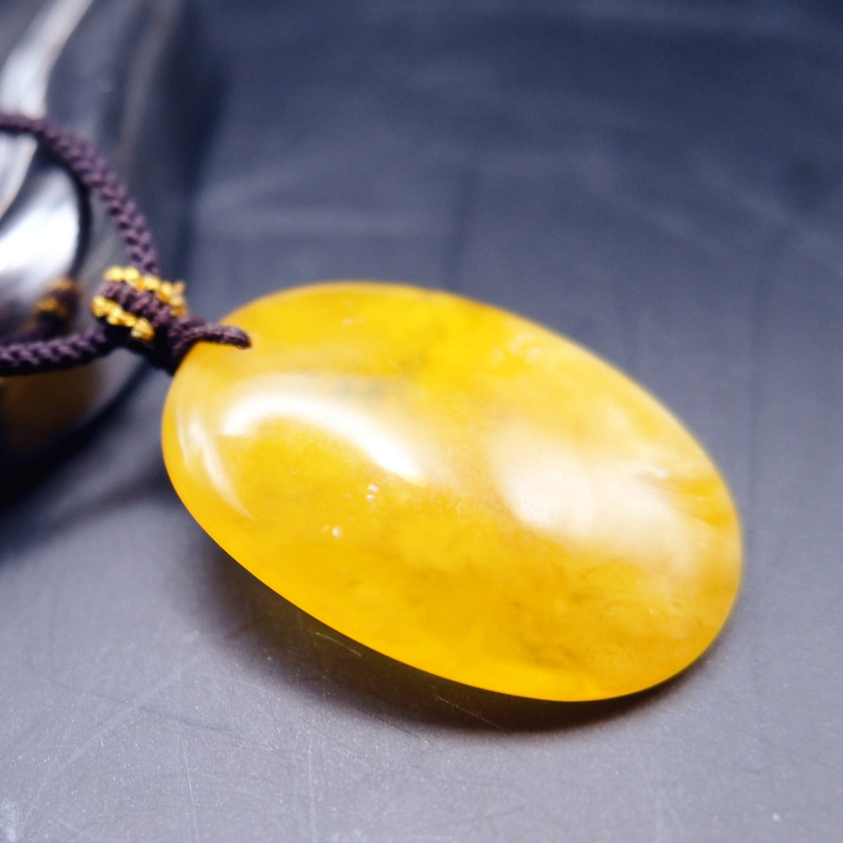 Pendant: yellow Baltic amber oval with cloudy white patches, dark cord, lying flat