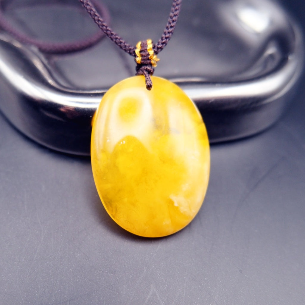 Pendant: yellow Baltic amber oval with cloudy white patches, dark cord, standing, reverse side