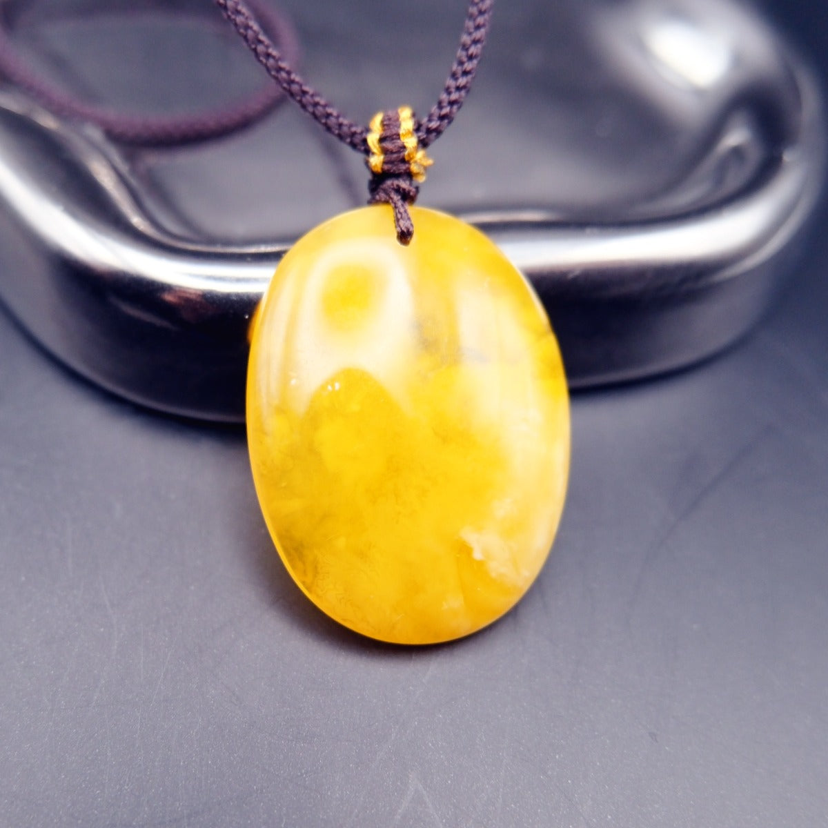 Pendant: yellow Baltic amber oval with cloudy white patches, dark cord, standing, reverse side