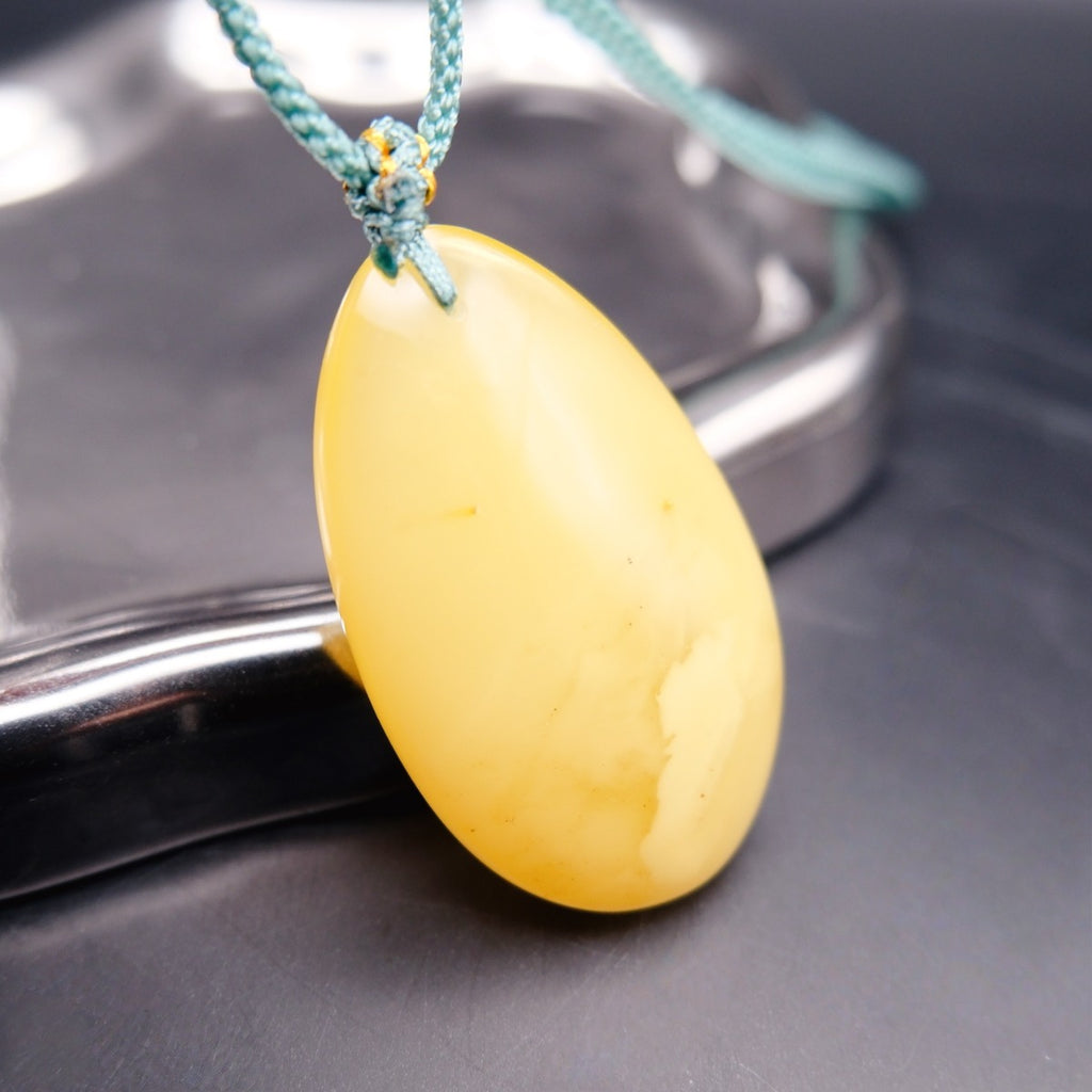 Pendant: pale opaque yellow Baltic amber oval drop, teal cord, reverse side