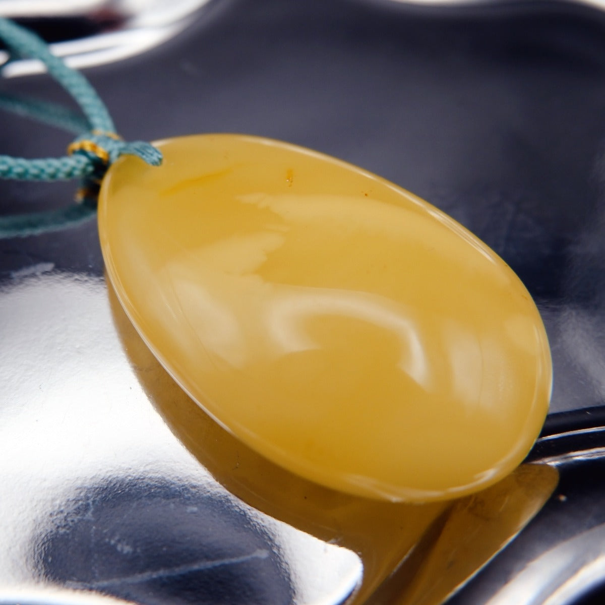 Pendant: pale opaque yellow Baltic amber oval drop, teal cord, side view