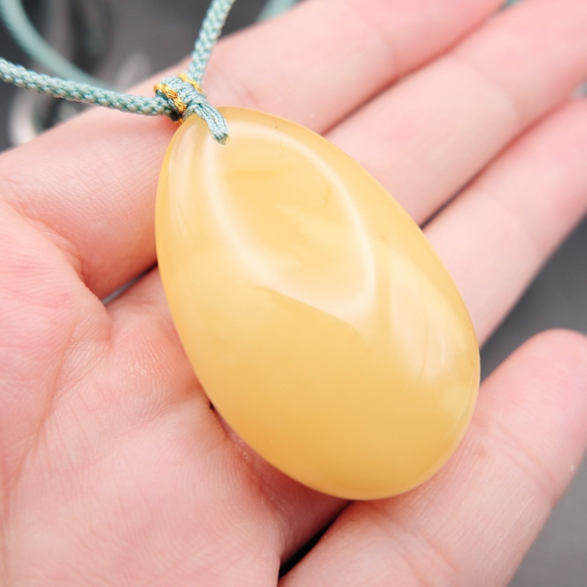 Pendant: pale opaque yellow Baltic amber oval drop, teal cord, on an open palm