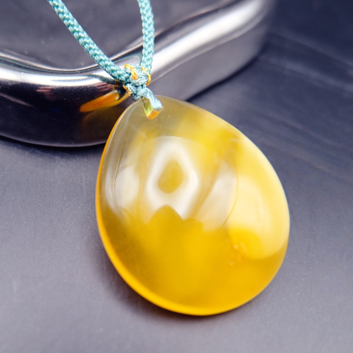Pendant: yellow Baltic amber teardrop, translucent top and opaque lower half, teal cord, closer view