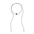 Pendant necklace: round brown-red tiger's eye bead on a long black cord with gold-coloured ribbed cone ends, white background
