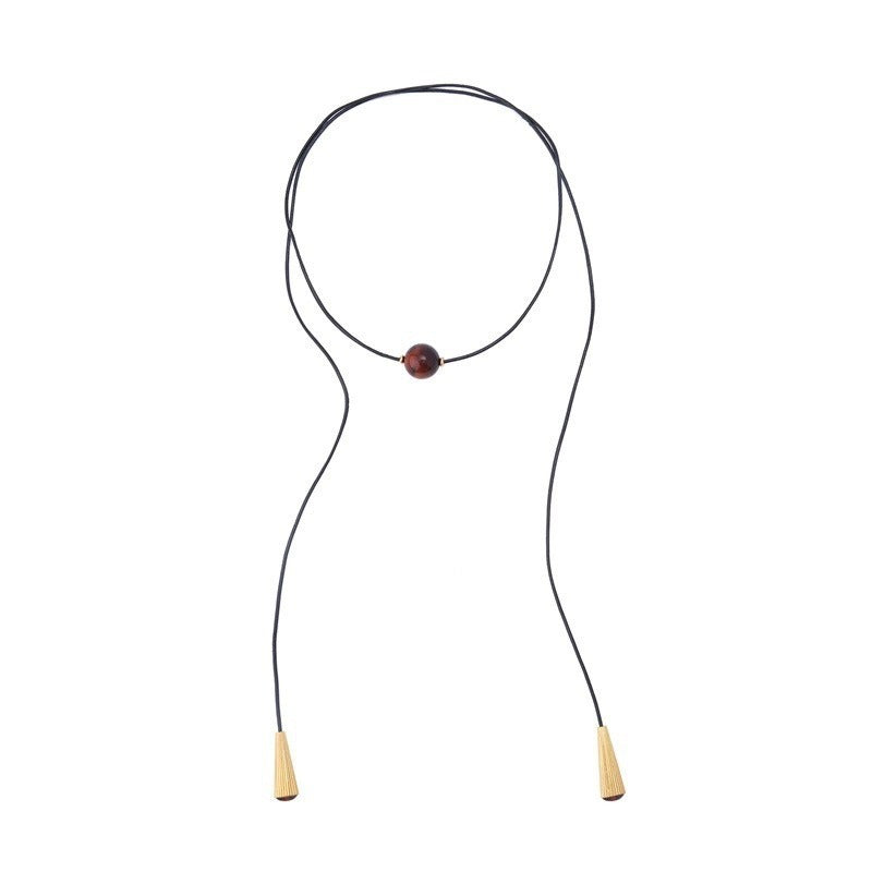 Pendant necklace: round brown-red tiger's eye bead on a long black cord with gold-coloured ribbed cone ends, white background