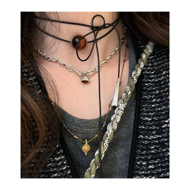 Pendant necklace tied at the neck: brown-red tiger's eye bead, black cord, silver-coloured cone end, among other necklaces
